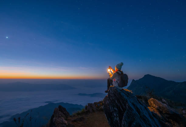 tourist woman holding a lantern while sitting on the rock on top of doi pha tang mountain a high cliff over the thai-laotian border located in wiang kaen district of chiang rai province of thailand. beautiful view before the 