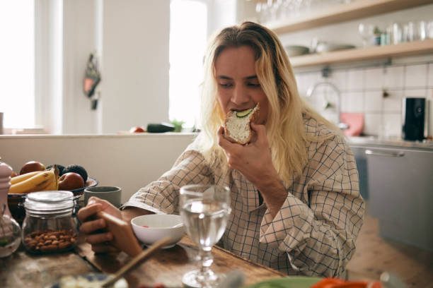 transgender person eating bread while watching mobile phone at home - food stock pictures, royalty-free photos & images