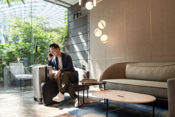 travelling asian businessman on his phone at an airport lounge - travel stock pictures, royalty-free photos & images