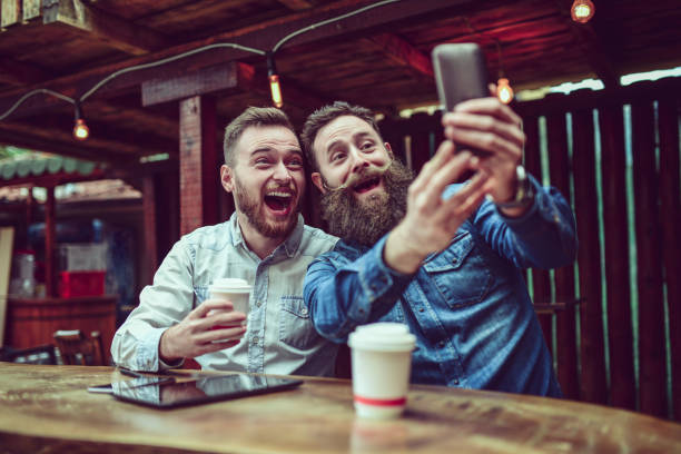 two bearded friends drinking coffee and taking selfie in restaurant - junk food stock pictures, royalty-free photos & images