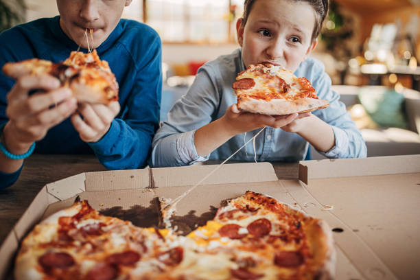 two brothers eating pizza together - junk food stock pictures, royalty-free photos & images