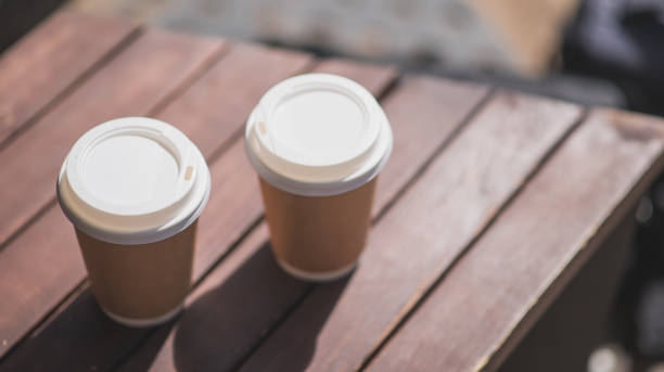 two coffees in paper disposable takeaway cups sit on a wooden table. coffee to take away, take it with you. - junk food stock pictures, royalty-free photos & images
