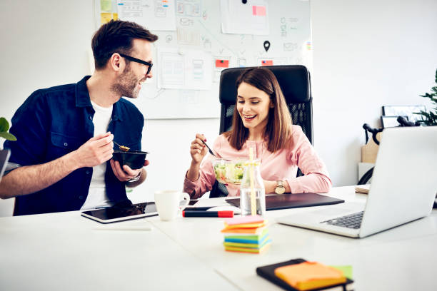 two colleagues talking during lunch break in office - junk food stock pictures, royalty-free photos & images