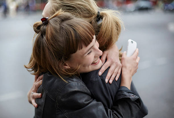 two female friends with cell phone hugging - hairstyle stock-fotos und bilder