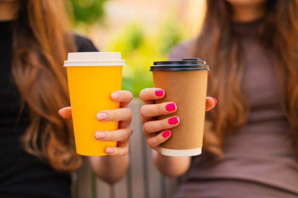 two female twin sisters hands holding recyclable takeaways coffee cup outdoors, close-up - junk food stock pictures, royalty-free photos & images