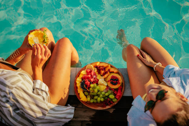 two friends eating fruits by the pool - food stock pictures, royalty-free photos & images