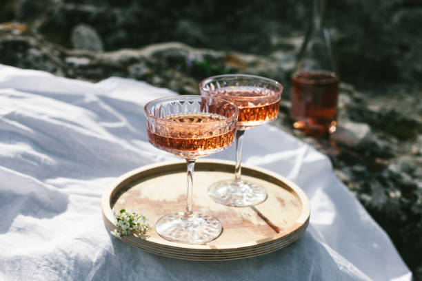 two glasses of rose wine outdoors on wooden tray and white textile, picnic in spring. sunny day, green grass and blossoming cherry trees. - home decoration stock pictures, royalty-free photos & images