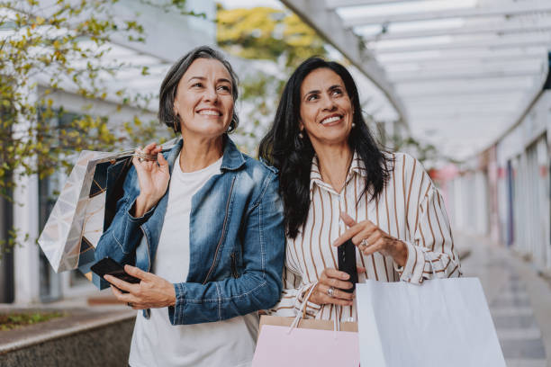 two mature friends shopping at the mall holding bags - fashion stock pictures, royalty-free photos & images
