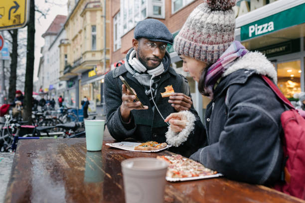 two mature students chatting over pizza slice on lunchbreak together - junk food stock pictures, royalty-free photos & images