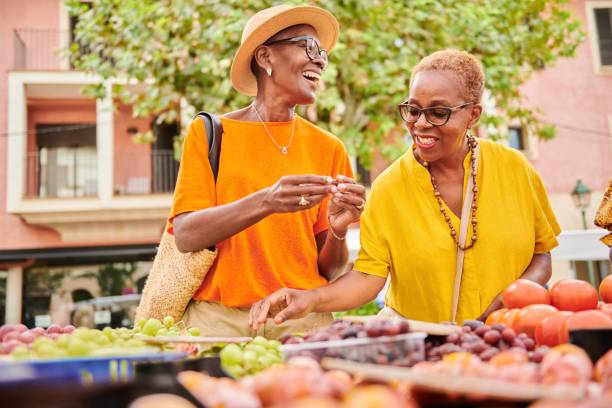 two mature women shopping together at an outdoor food market - travel stock pictures, royalty-free photos & images