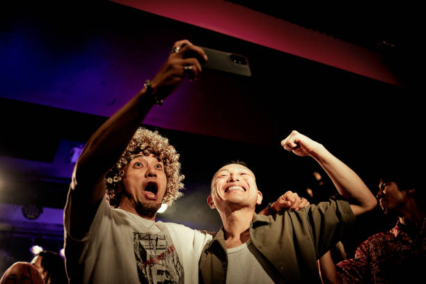two men taking selfies with their cell phones at a live music club. - concert stock pictures, royalty-free photos & images