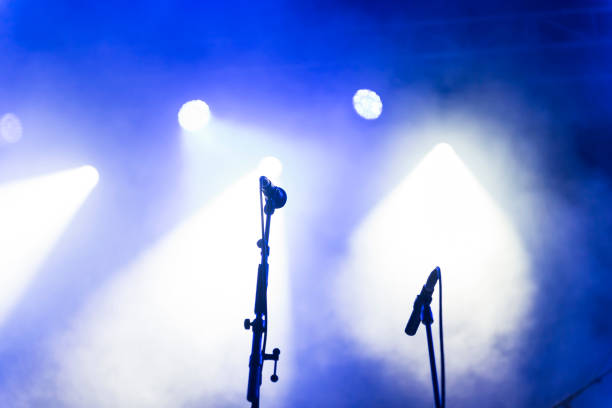 two microphone stands on a stage, under blue theatrical smoke and spotlights - concert stockfoto's en -beelden