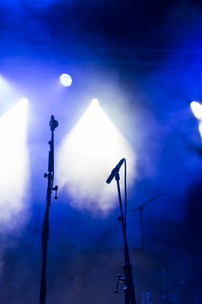 two microphones stands on a concert stage under blue and white spotlights - concert stock pictures, royalty-free photos & images