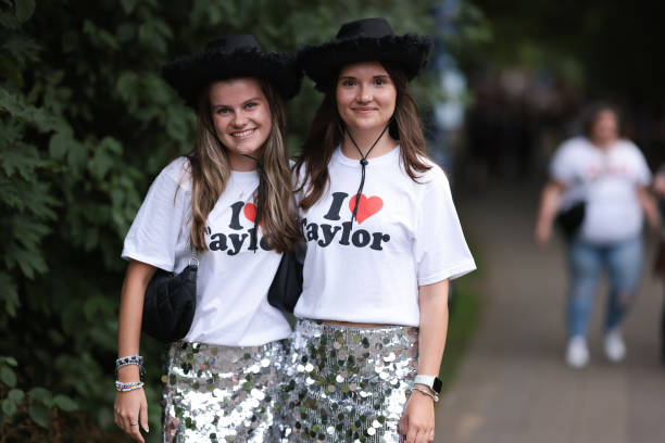 Two Taylor Swift fans are seen wearing matching outfits, consisting of black cowboy hats, white “I love Taylor” t-shirts, silver glitter mini skirts,...