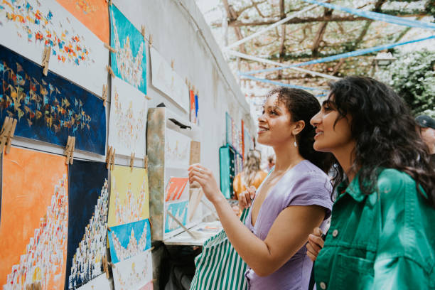 two woman admire paintings at a market stall as they vacation in europe - travel stock pictures, royalty-free photos & images