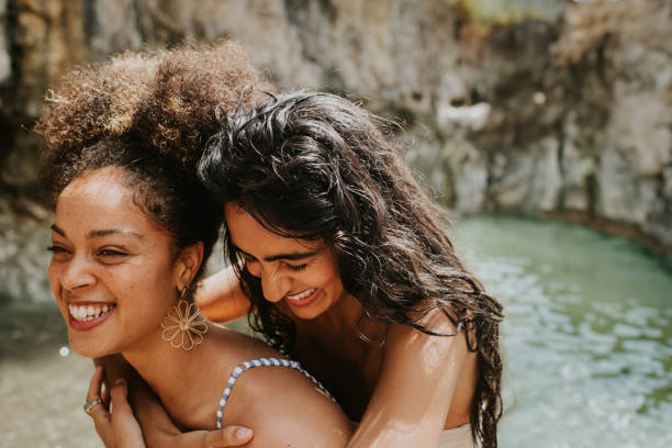 two woman affectionately embrace in the ocean, one drapes her arms around her female friend and they laugh. - travel stock pictures, royalty-free photos & images