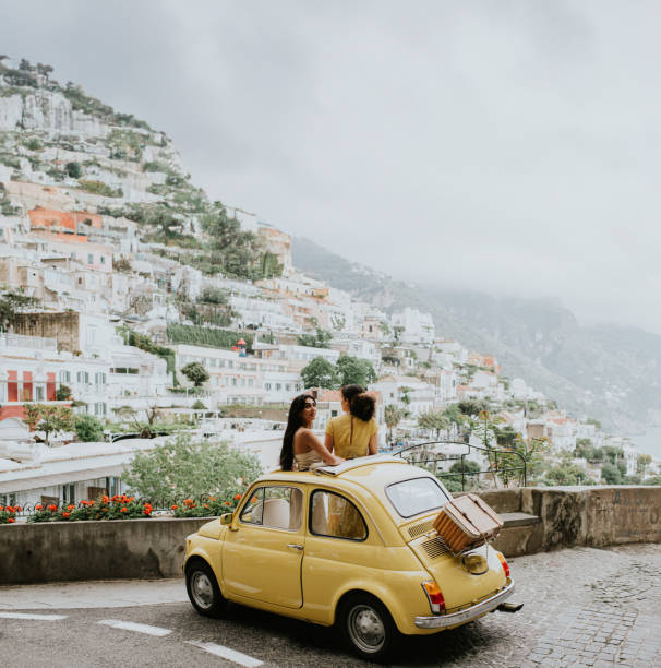 two woman stand in a vintage yellow fiat, and admire the view of positano, italy. - travel stock-fotos und bilder
