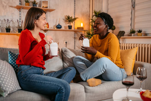 two women eating ordered food together at home - junk food stock pictures, royalty-free photos & images