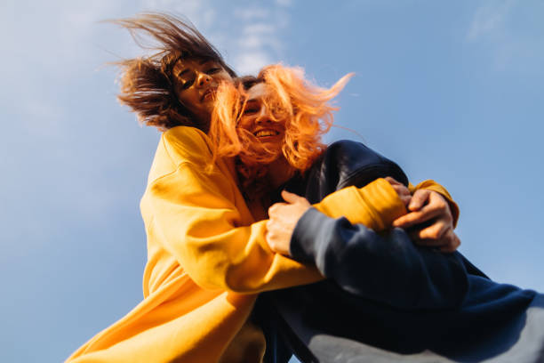 two women hugging at the blue sky background at the sunset - fashion stock pictures, royalty-free photos & images
