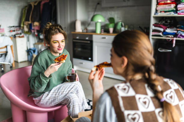 two young housemates eat pizza they ordered from outside together at home - junk food stock pictures, royalty-free photos & images