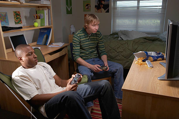 two young men playing video game in dorm room - junk food stockfoto's en -beelden