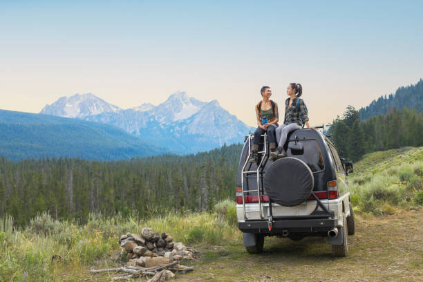 two young woman on top of camper van in remote mountain landscape - travel stock pictures, royalty-free photos & images