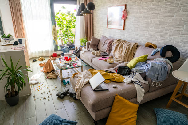 upset woman head in hands contempling her messy and dirty living room - junk food stock pictures, royalty-free photos & images