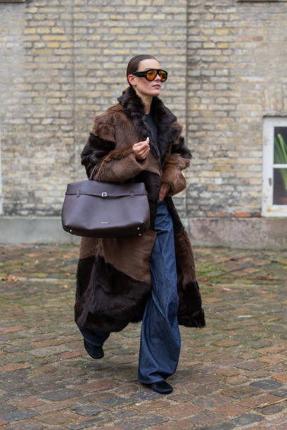 Vera van Erp wears brown black two tone fur coat, Manu Atelier bag, denim jeans, sunglasses outside TG Botanical during the Copenhagen Fashion Week...