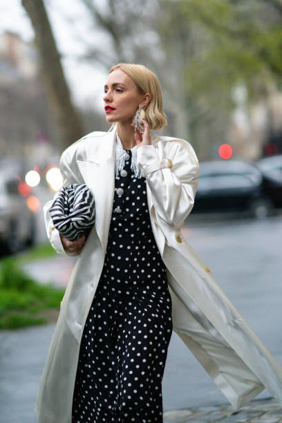 Viktoria Rader wears long bejeweled earrings, a white long coat, a black and white zebra print puff bag, a black and white dress with polka dots,...