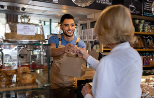 waiter giving a paper bag to a client buying pastries at a cafe - junk food stock pictures, royalty-free photos & images