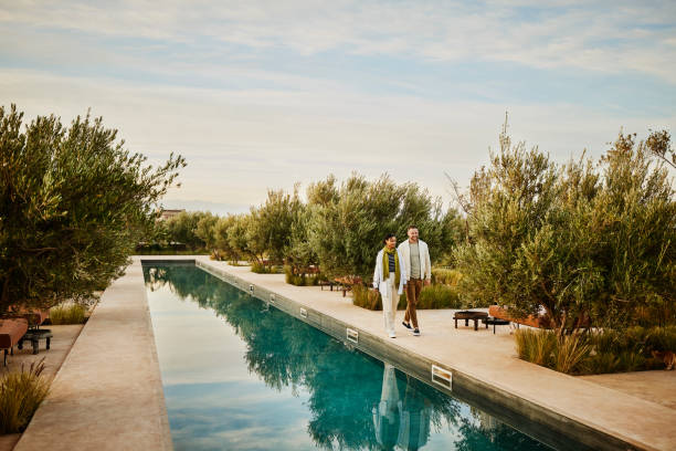 wide shot couple walking along edge of pool at boutique luxury resort - travel stock pictures, royalty-free photos & images