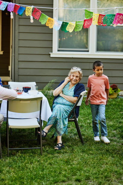 wide shot grandmother at table in backyard during family birthday party - garden decoration stock pictures, royalty-free photos & images