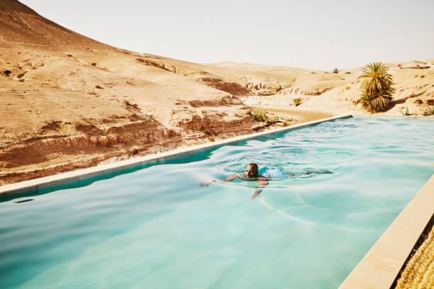 wide shot man swimming in pool at moroccan desert camp during vacation - travel stock pictures, royalty-free photos & images
