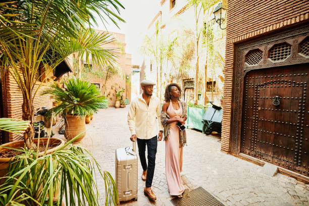 wide shot of couple arriving in hotel courtyard with rolling luggage - travel stock pictures, royalty-free photos & images