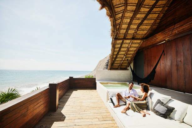 wide shot of couple relaxing on deck of luxury tropical villa overlooking ocean - travel stock pictures, royalty-free photos & images