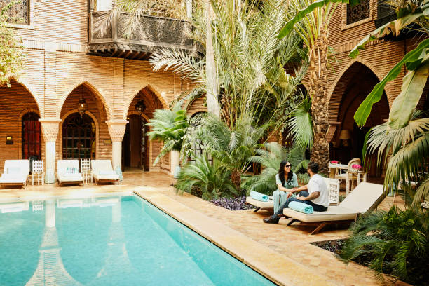 wide shot of couple sitting by pool in courtyard of luxury hotel - travel stock pictures, royalty-free photos & images