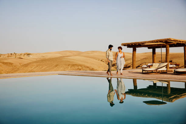 wide shot of couple walking around pool at desert camp at sunrise - travel stock pictures, royalty-free photos & images