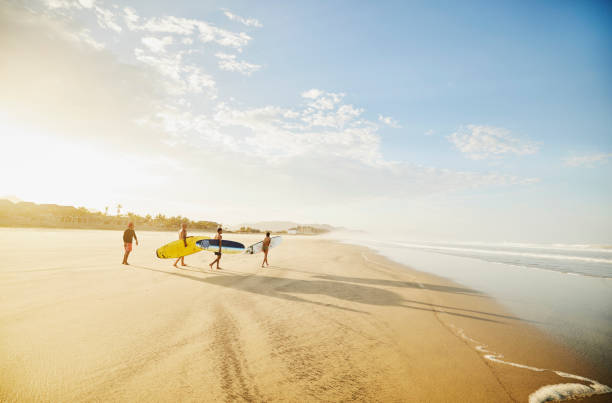 wide shot of family carrying surfboards while taking surf lesson - travel stock pictures, royalty-free photos & images