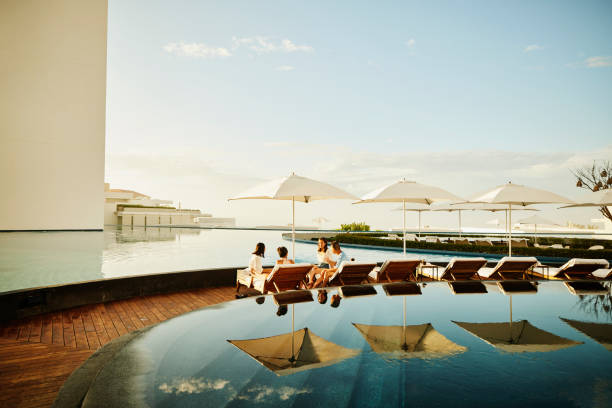wide shot of family hanging out on lounge chairs by pool at resort - travel stock pictures, royalty-free photos & images
