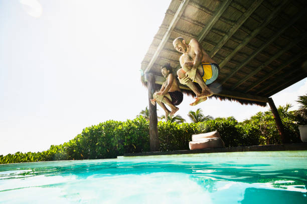 wide shot of gay couple jumping into pool at luxury tropical villa while on vacation - travel photos et images de collection