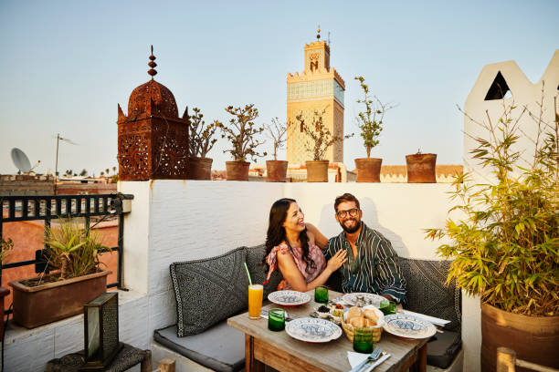 wide shot of laughing couple dining at rooftop restaurant in marrakech - travel stock pictures, royalty-free photos & images