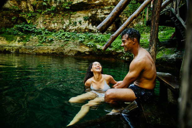 wide shot of laughing couple hanging out on stairs into cenote after swimming - travel stock pictures, royalty-free photos & images