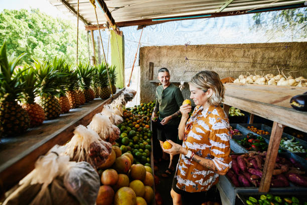 wide shot of smiling woman smelling fruit while shopping at local market during vacation - travel stock pictures, royalty-free photos & images