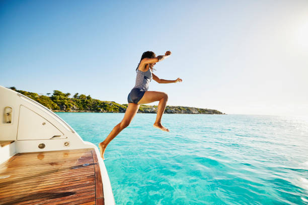 wide shot of teenage girl jumping off swim step of yacht into ocean - travel stock-fotos und bilder