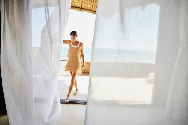 wide shot of woman walking through curtains on deck of luxury suite at tropical resort - travel stock pictures, royalty-free photos & images
