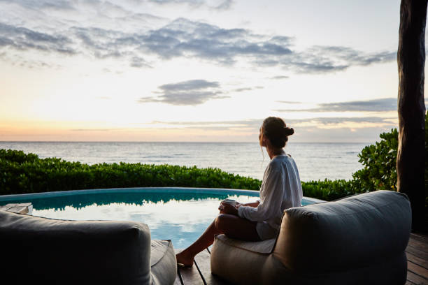 wide shot of woman watching sunrise while sitting poolside at luxury suite at tropical resort - travel stock-fotos und bilder