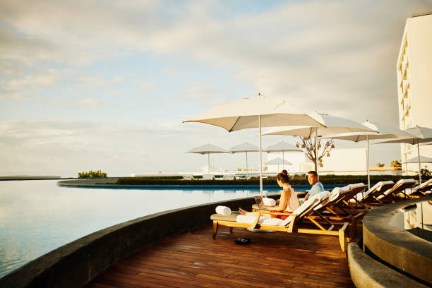 wide shot of woman working on laptop in lounge chair by pool at resort - travel stock pictures, royalty-free photos & images