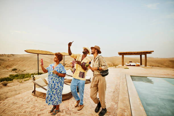 wide shot smiling friends taking selfies by pool at desert camp - travel stock pictures, royalty-free photos & images