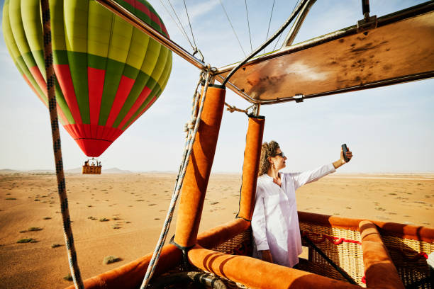 wide shot woman taking selfie during sunrise hot air balloon ride - travel stock-fotos und bilder