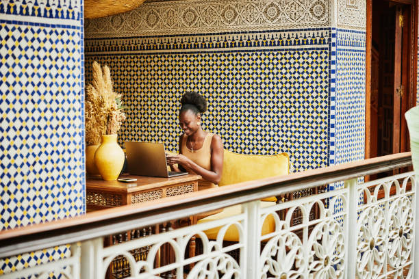 wide shot woman working on laptop in alcove of ornately decorated riad - travel stockfoto's en -beelden